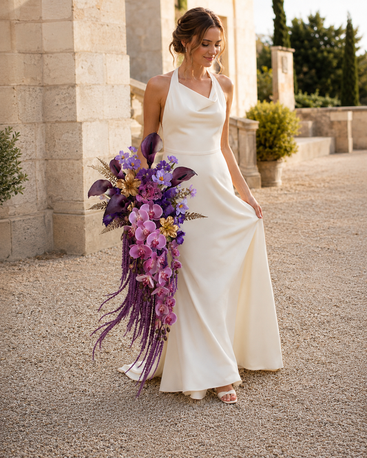 Bride holding the Gilded Amethyst plum calla lily and gold orchid bridal bouquet, full-length hero product shot against European-estate stone architecture