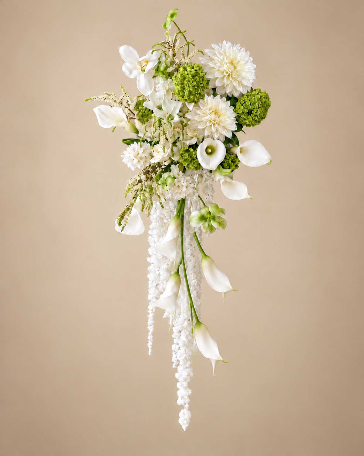 White Green Cascade bridal bouquet of white dahlias, white calla lilies and green hydrangea with trailing white blooms, shown on a beige background.