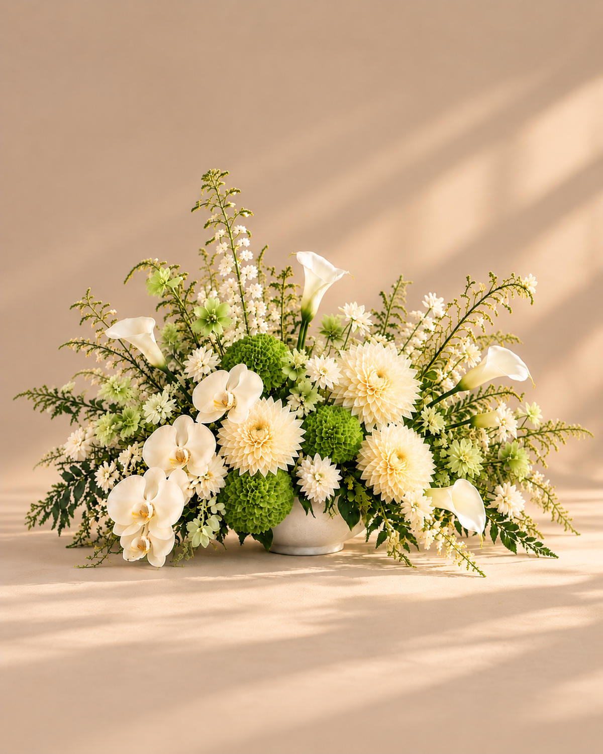 White Green Table Centerpiece with white orchids, cream dahlias, green hydrangea and white calla lilies in a white vase, shown against a beige background.