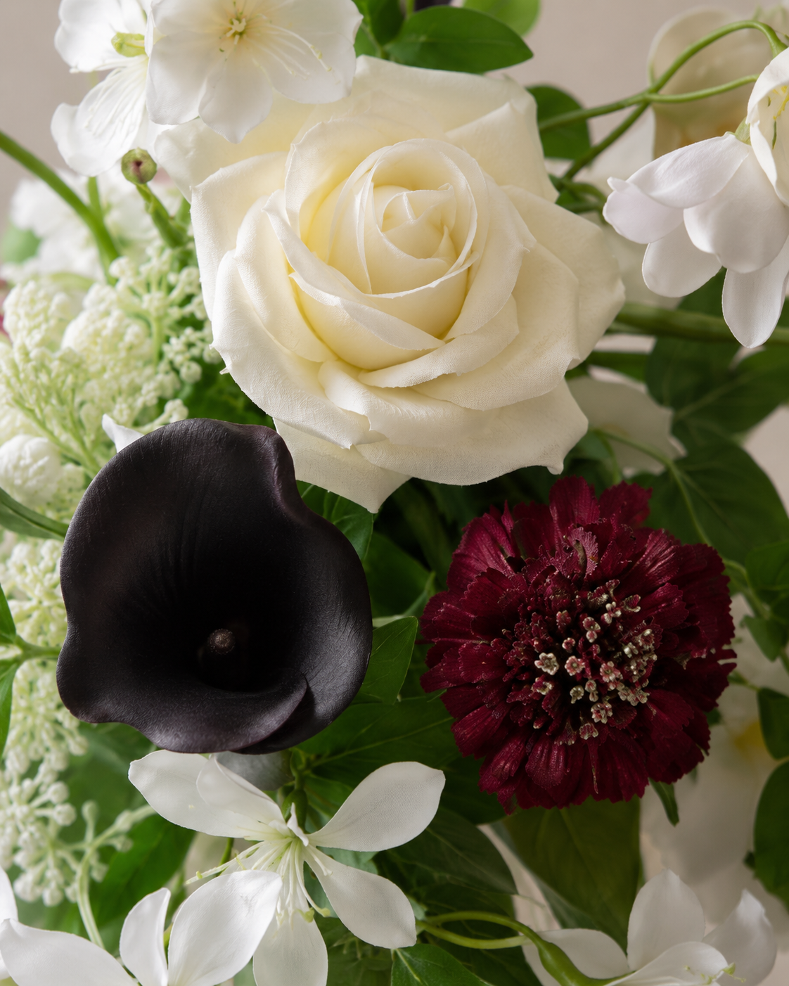 Close-up detail of the Ivory Noir bouquet showing an ivory garden rose, plum calla lily, burgundy scabiosa and white filler flowers