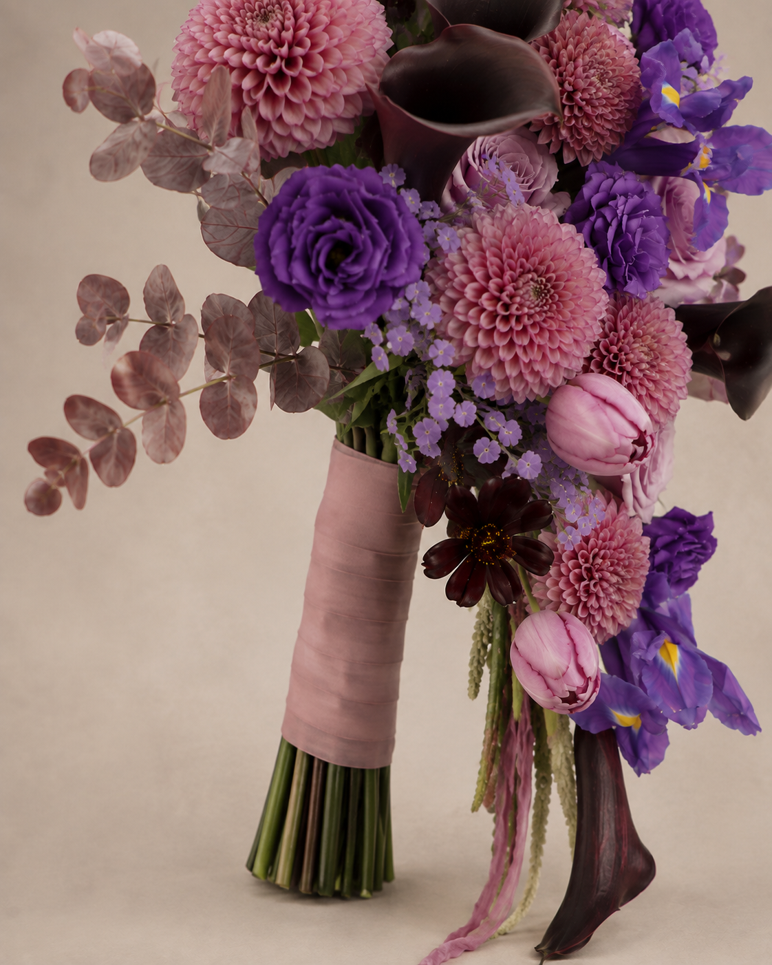 Close-up of the wrapped bouquet handle with dusty pink dahlias, violet irises, black calla lilies, lisianthus, tulips, dark cosmos and cascading botanical accents